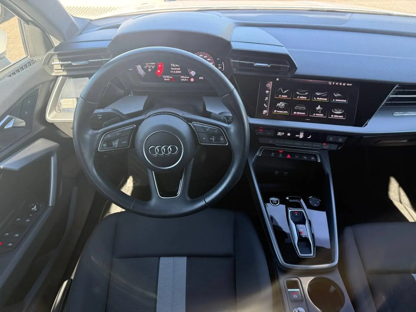 Vue intérieure frontale de l'Audi A3 Sportback 2024, volant cuir noir, écran tactile et console centrale brillante.