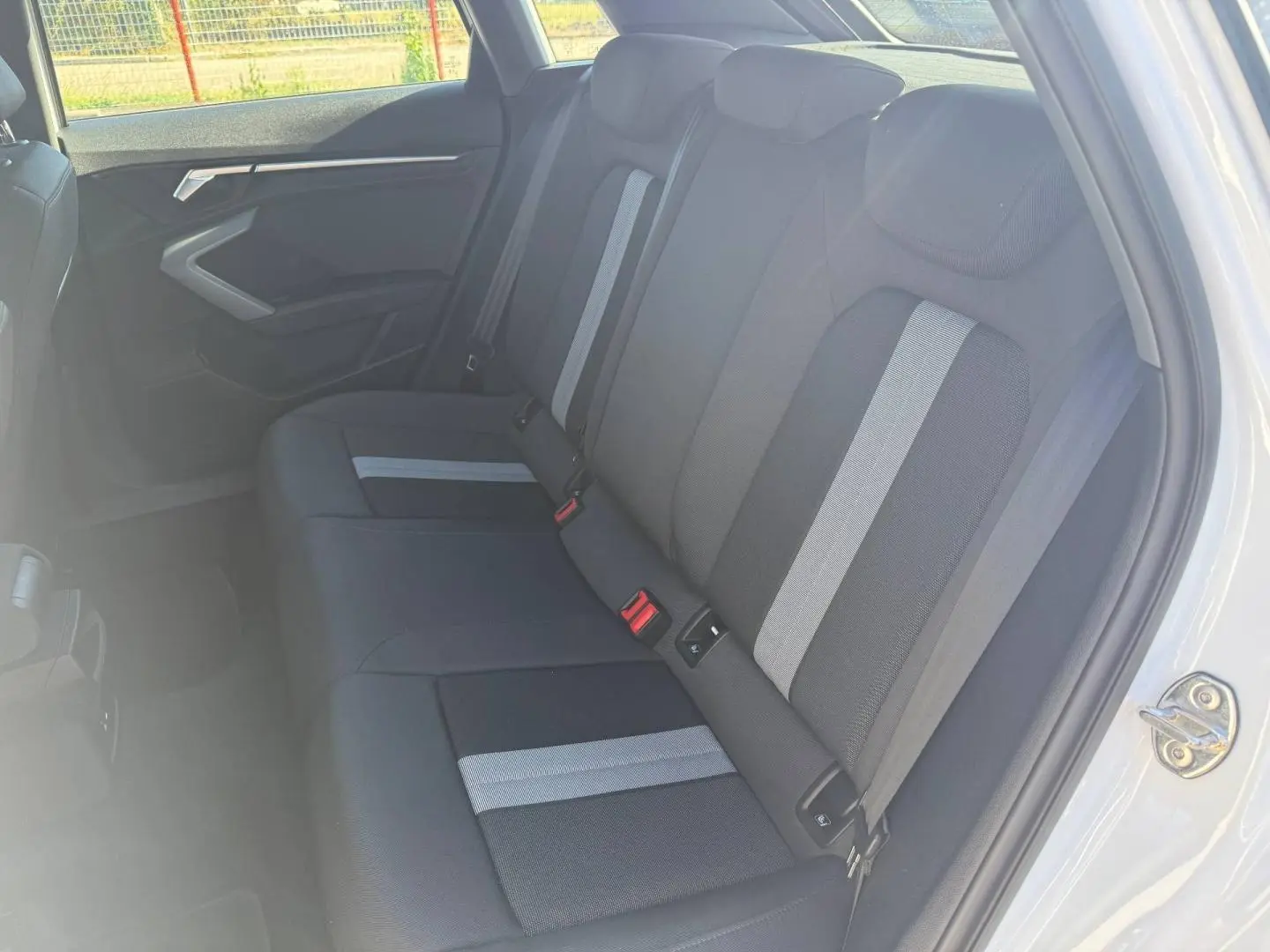 Vue intérieure côté droit des sièges arrière en tissu noir avec bandes grises de l'Audi A3 Sportback 2024 blanche.