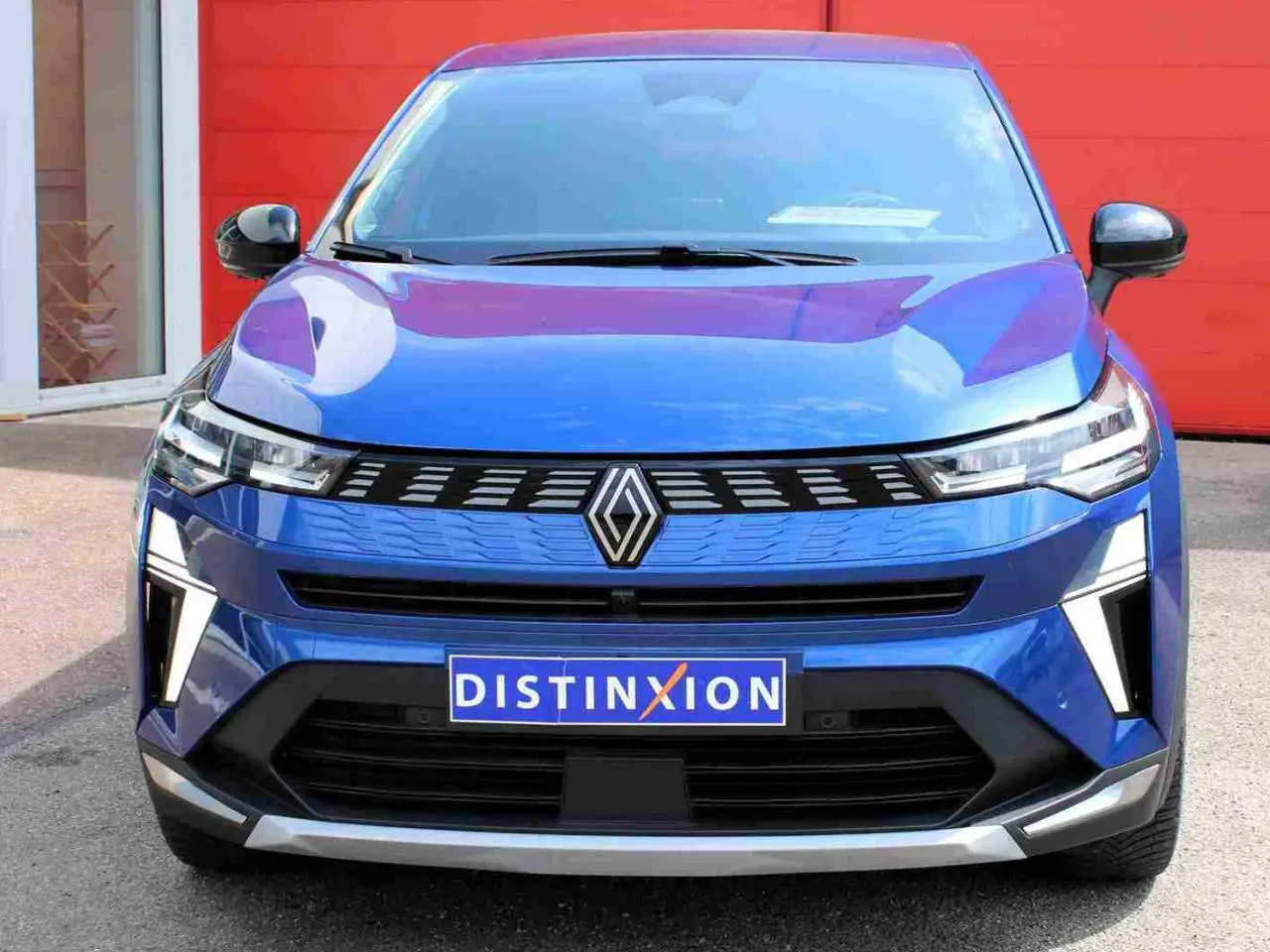 Vue avant d'une Renault Symbioz 2025 bleu Iron avec calandre 3D et feux LED distinctifs sur fond rouge.