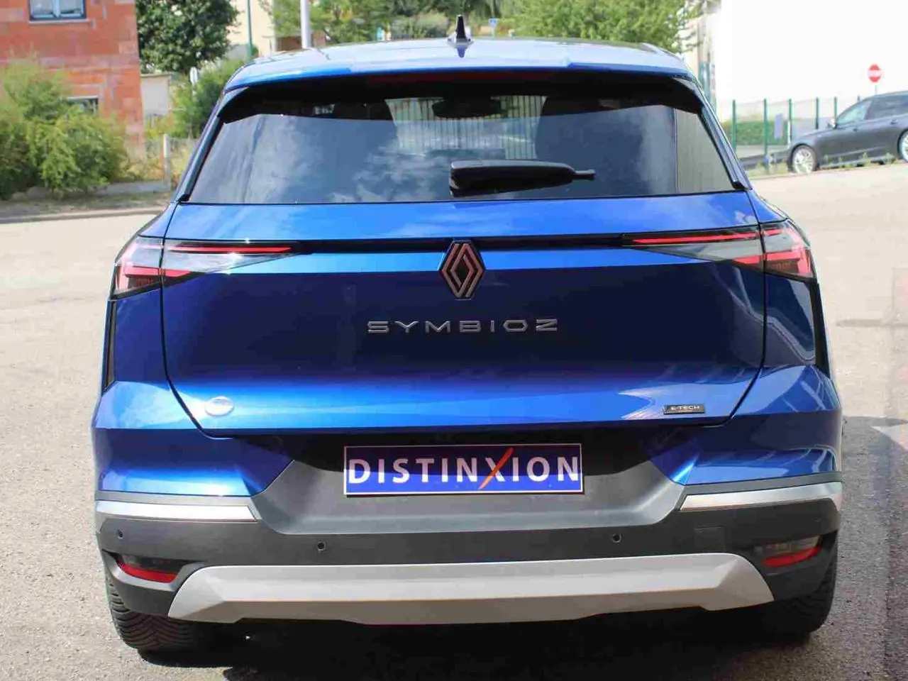 Vue arrière d’un Renault SYMBIOZ bleu avec feux LED fins et logo central, sur un parking extérieur.