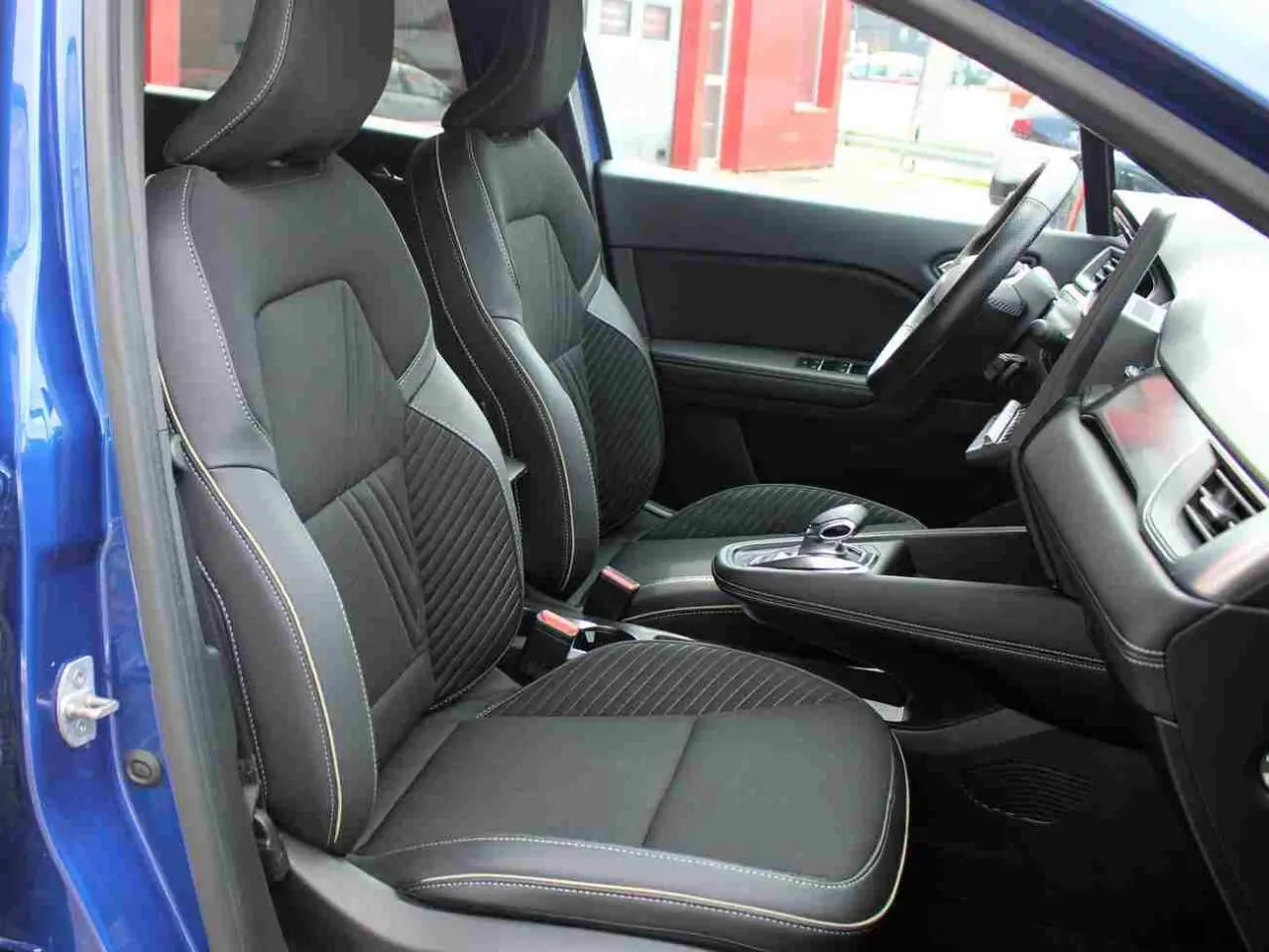 Vue intérieure côté conducteur de la Renault Symbioz 2025 bleu, sièges noirs avec surpiqûres contrastées et console centrale moderne.