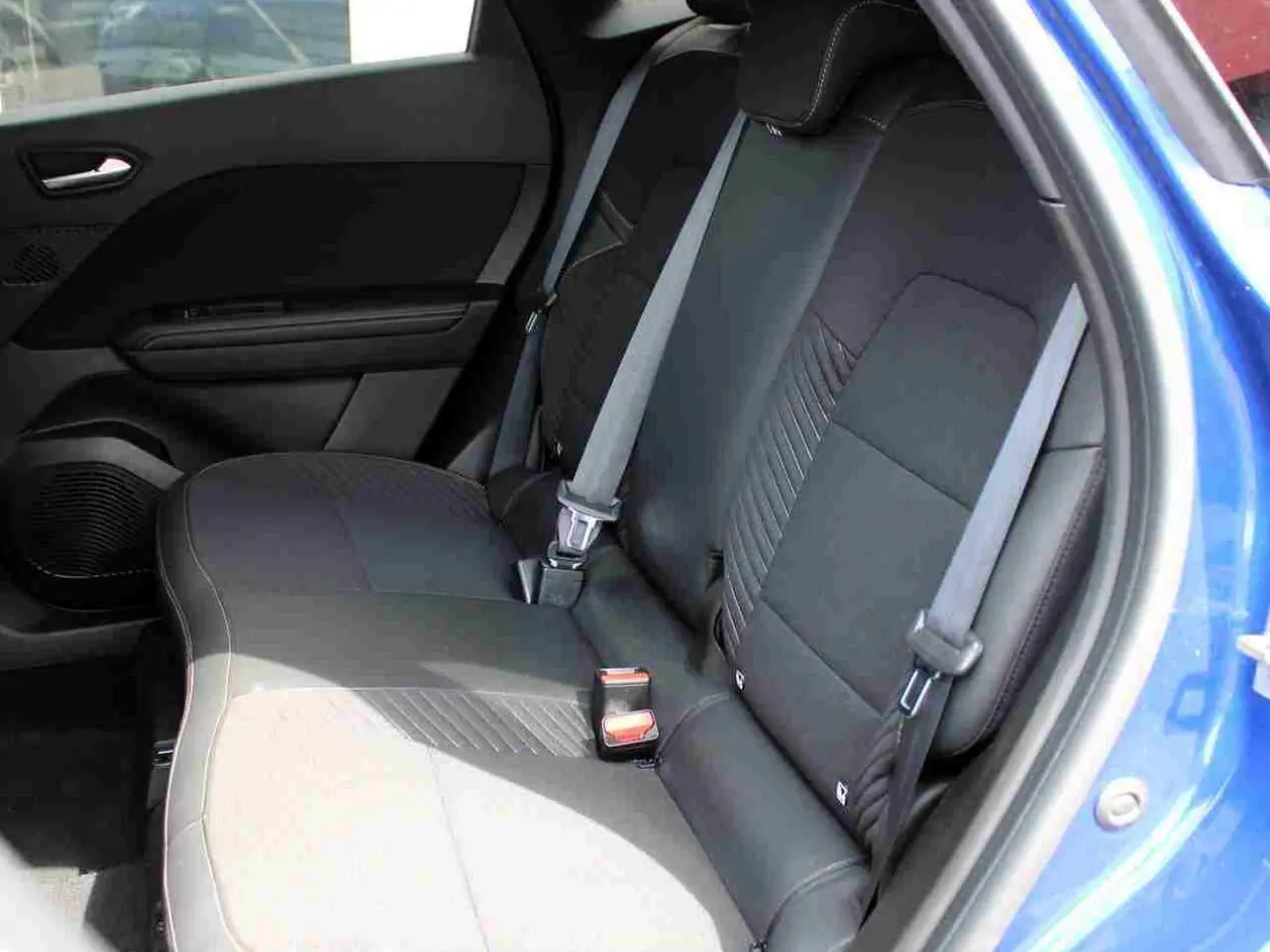 Vue intérieure sur la banquette arrière noire du Renault Symbioz bleu, avec ceintures de sécurité et porte côté droit ouvert.