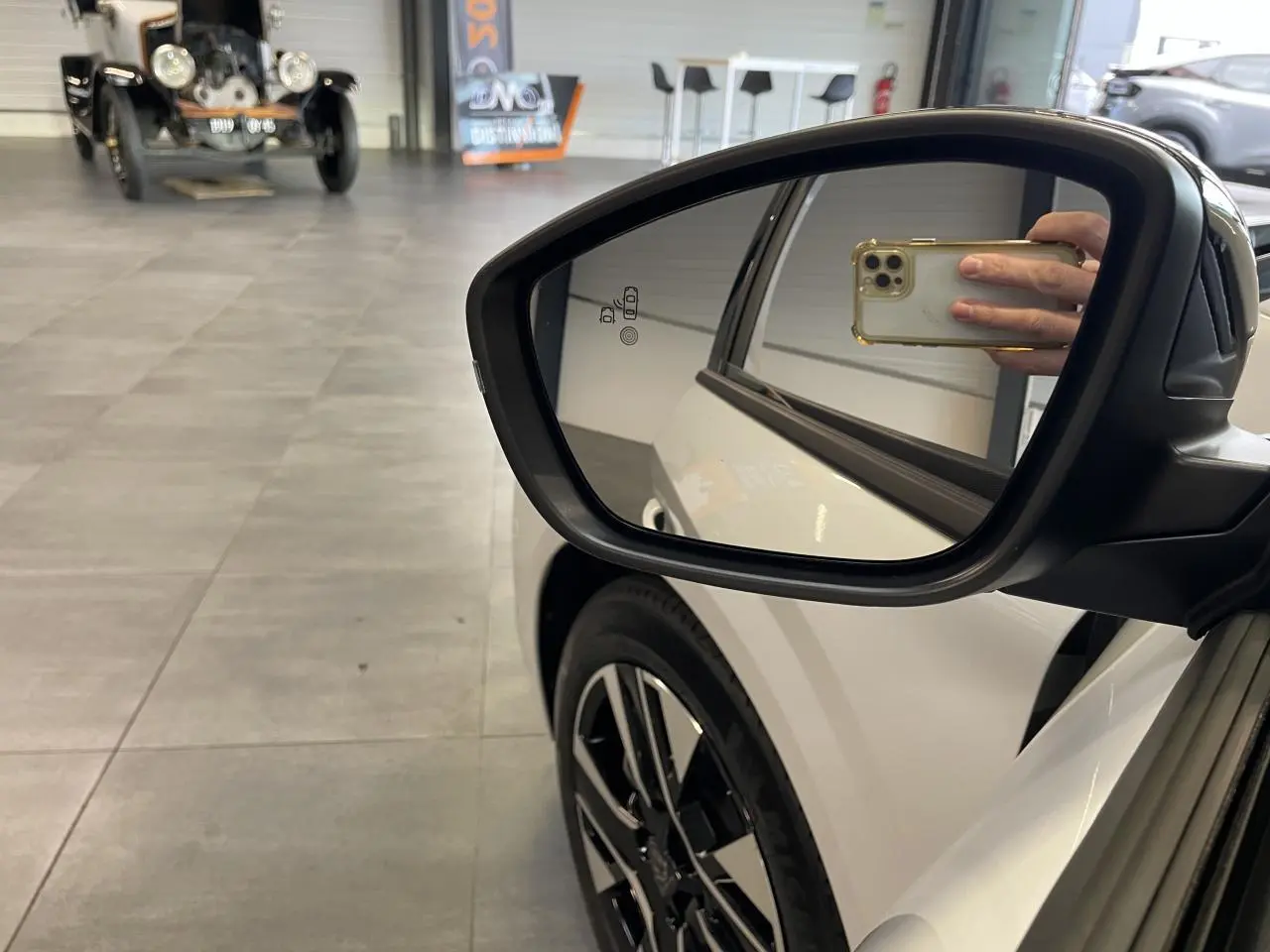 Rétroviseur droit d’une Peugeot 208 blanche Okenite, avec jante alliage 16’’ et reflet intérieur visible.