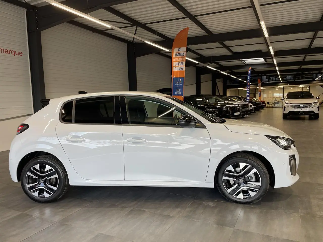 Peugeot 208 blanche okenite vue de profil côté gauche en intérieur avec jantes alliage bi-tons et rétroviseurs noirs.