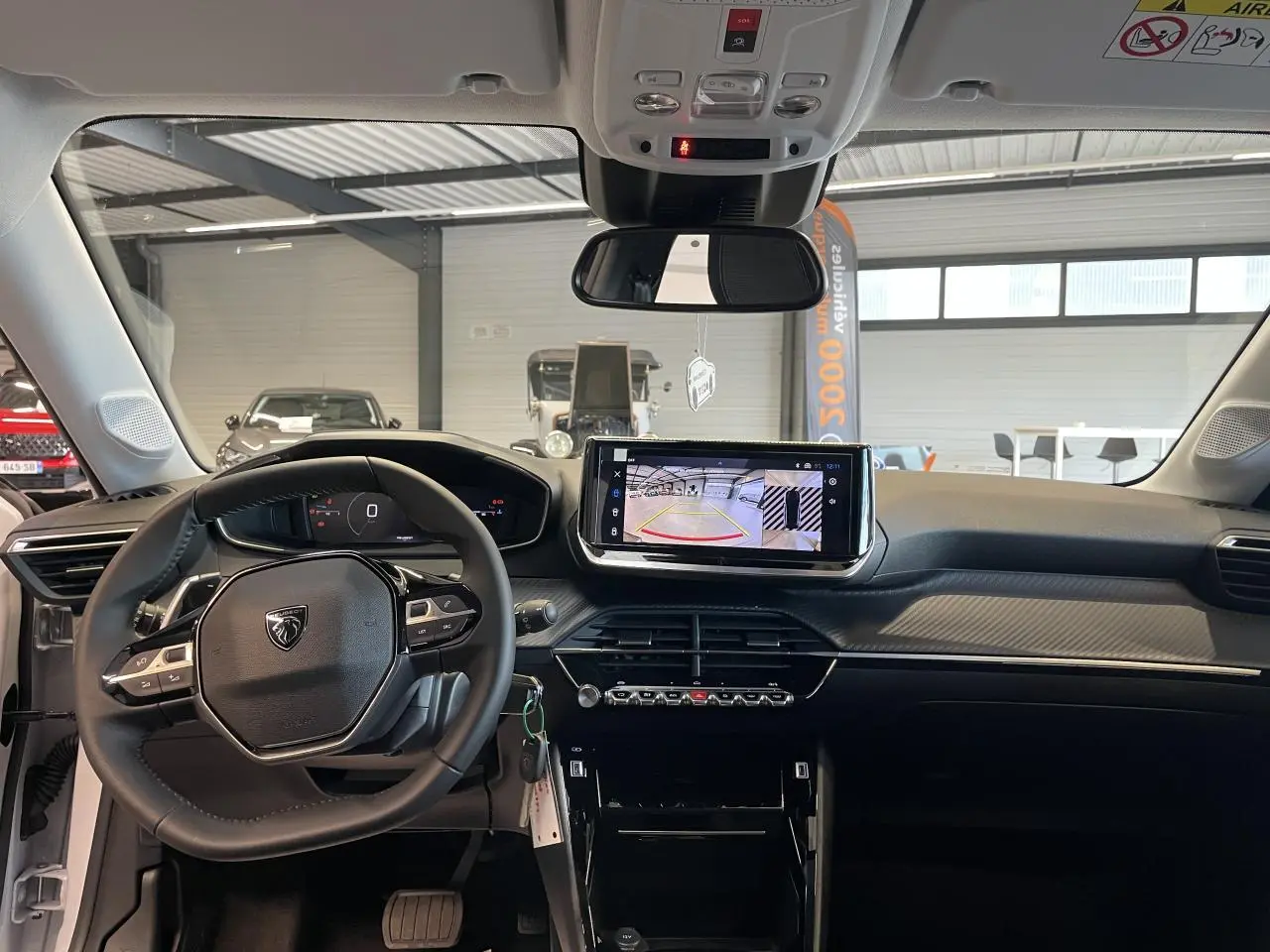 Vue intérieure avant du tableau de bord noir et gris clair de la Peugeot 208 hybride 2025 avec écran tactile et volant compact cuir.