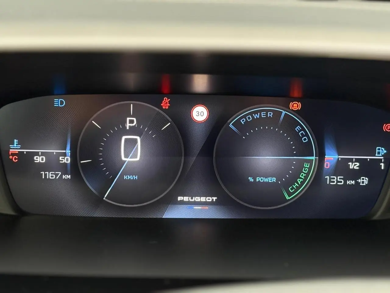 Tableau de bord numérique Peugeot 308 SW Hybrid 2025 affichant vitesse à zéro et indicateurs de charge et température.