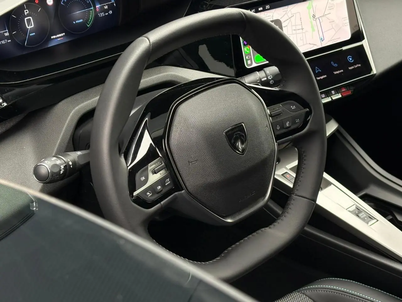 Vue rapprochée du volant noir du Peugeot 308 SW Hybrid 2025 avec tableau de bord numérique et écran tactile.