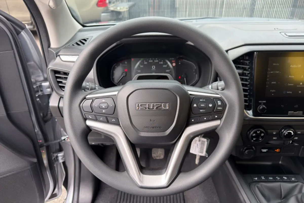 Vue intérieure centrée sur le volant multifonctions noir de l'Isuzu D-MAX 2026, avec tableau de bord et écran tactile visibles.