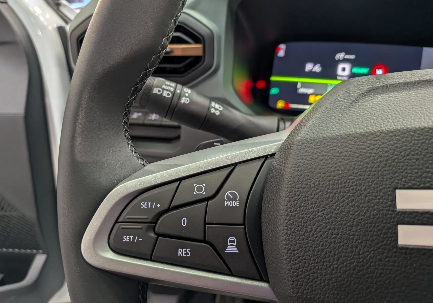 Gros plan sur la partie gauche du volant noir du Dacia Bigster Hybrid-G 150, avec commandes de régulateur et tableau de bord numérique flou.
