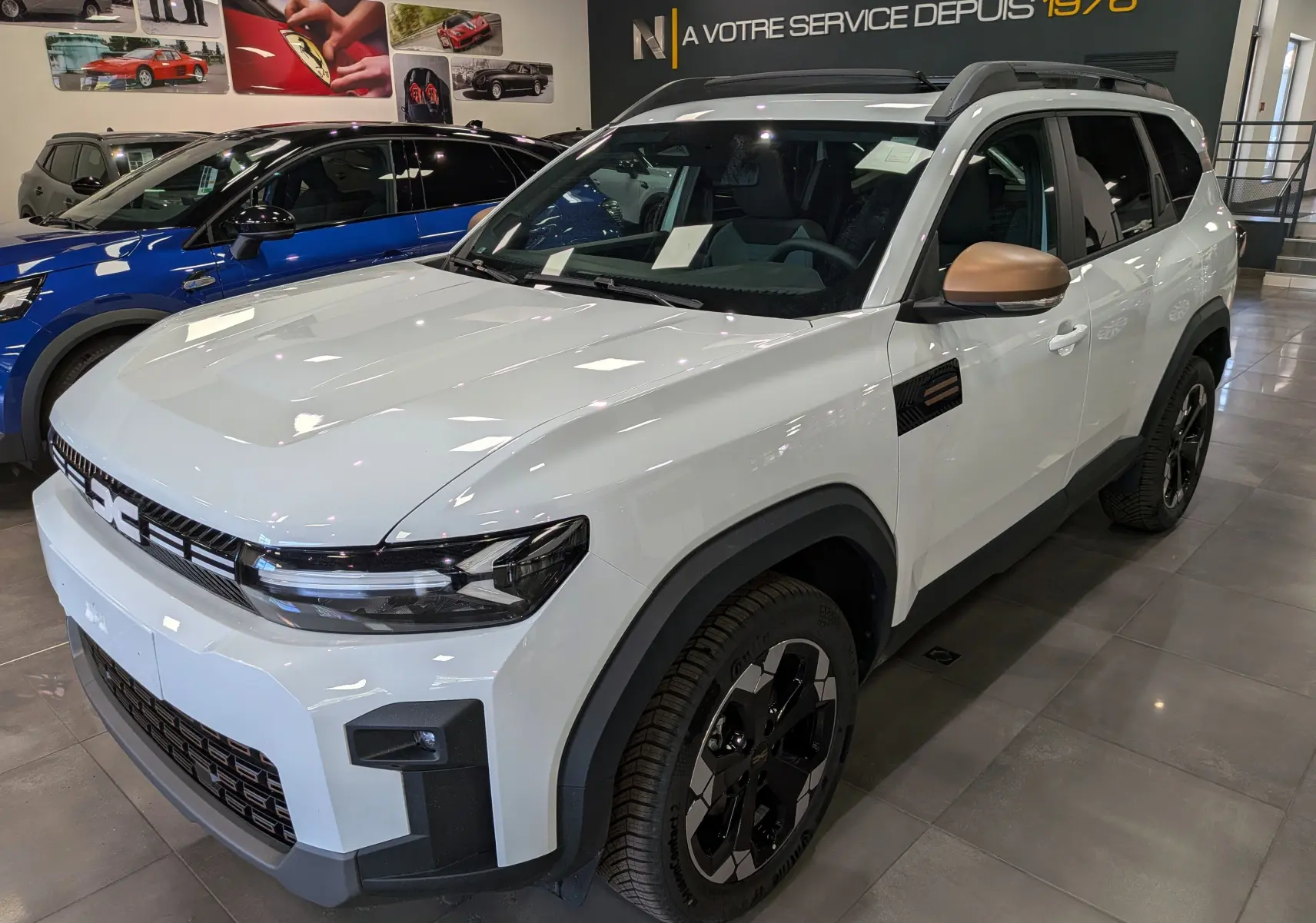 Vue 3/4 avant droite du Dacia Bigster blanc Glacier avec rétroviseurs bronze et jantes biton noir en showroom.