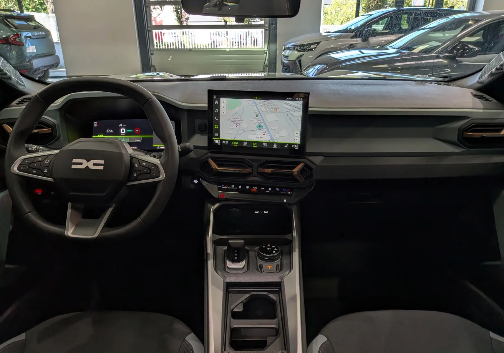 Vue intérieure frontale du tableau de bord du Dacia Bigster Hybrid-G 150 4x4 blanc glacier avec écran tactile central et volant multifonction.