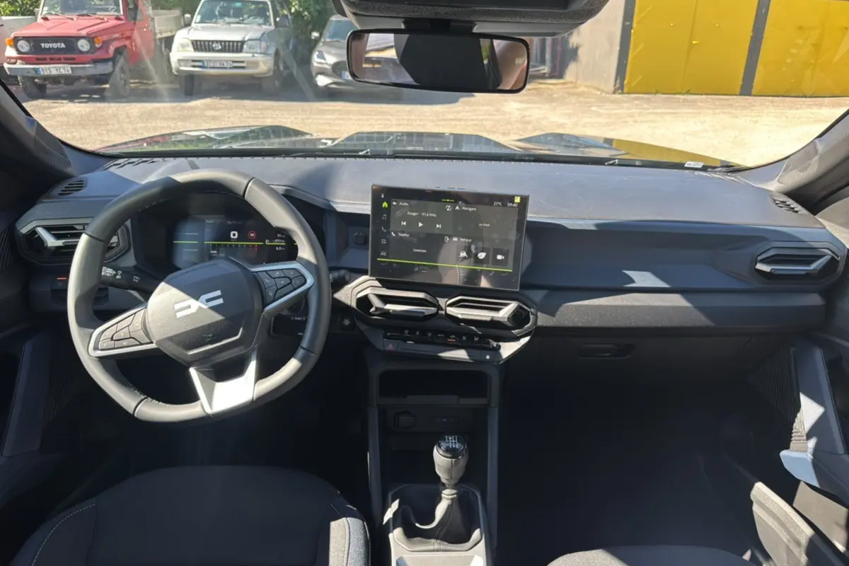 Vue intérieure avant du Dacia Bigster TCE 130 4x4 vert cèdre, avec tableau de bord moderne et écran tactile central.