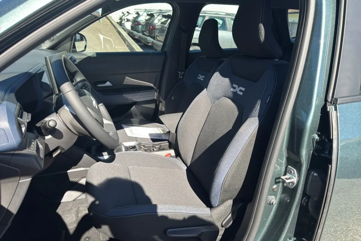 Vue intérieure côté conducteur du Dacia Bigster vert cèdre, montrant les sièges avant avec logo DC et volant cuir soft feel.