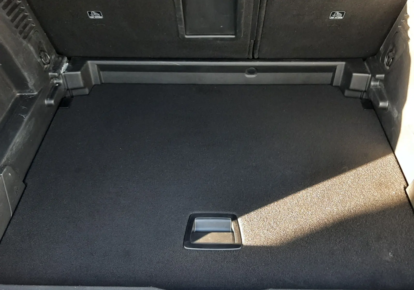 Vue plongeante sur le coffre vide du Peugeot 3008 gris platinium, montrant le tapis de sol et l'accès au rangement sous plancher.
