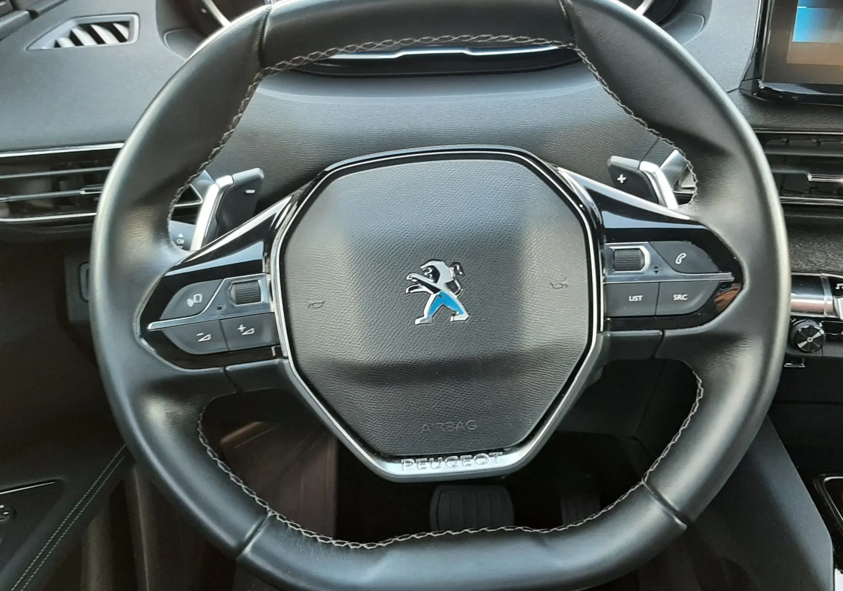 Vue rapprochée du volant noir du Peugeot 3008 2023 avec commandes intégrées et tableau de bord numérique en arrière-plan.