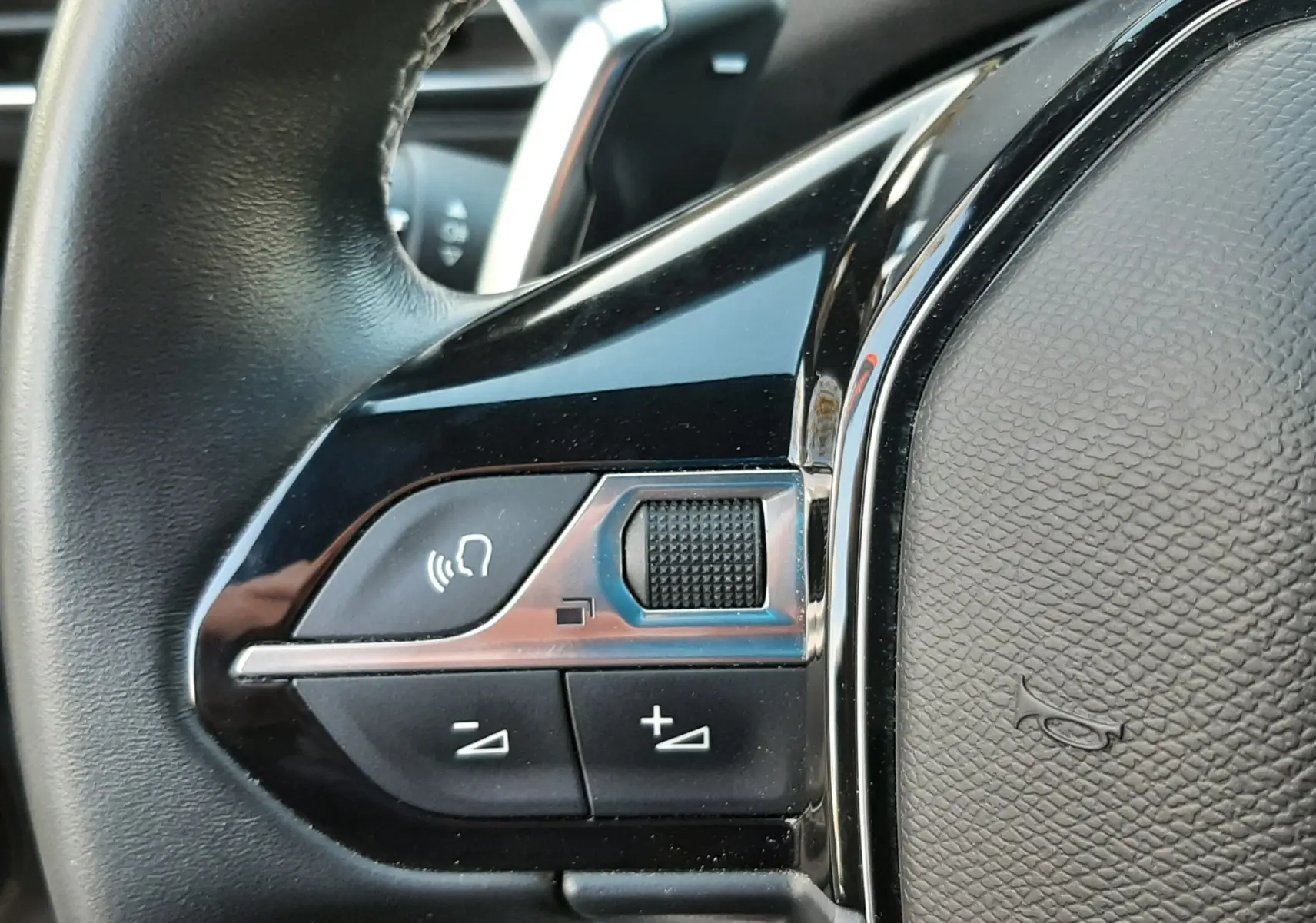 Gros plan sur les commandes gauche du volant en cuir noir du Peugeot 3008 gris platinium, avec boutons de volume et commande vocale.