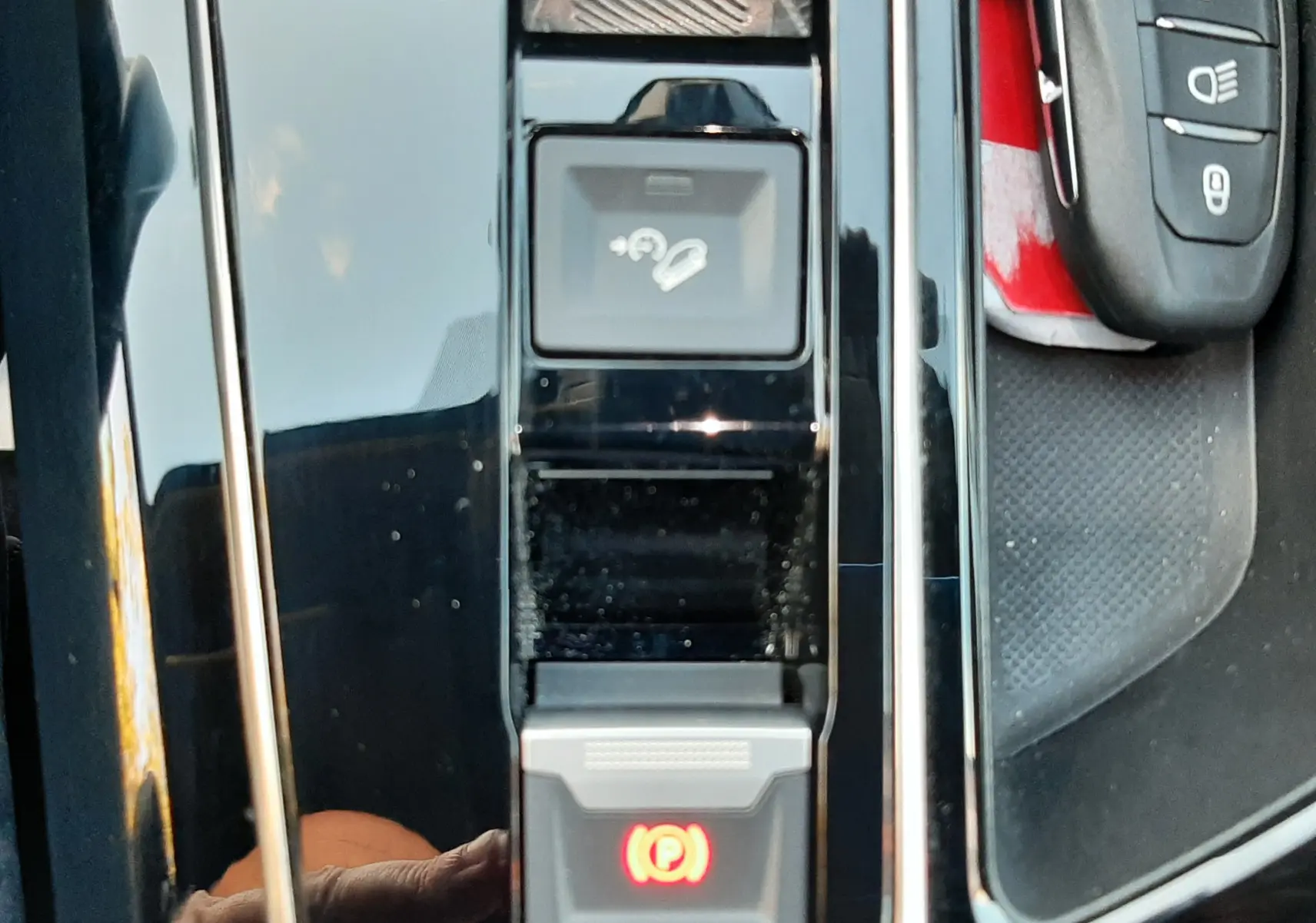Gros plan sur la console centrale noire brillante du Peugeot 3008 2023 avec bouton frein à main électronique allumé et clé de contact.