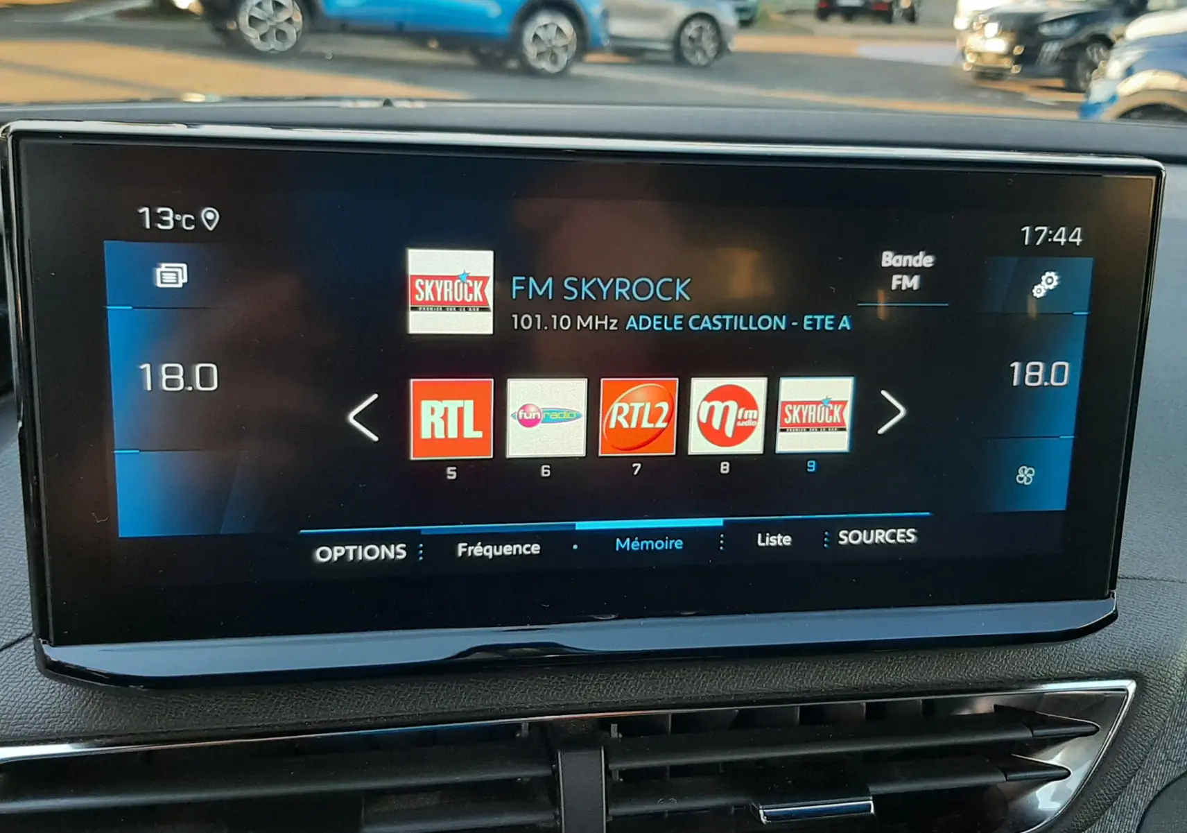 Écran central tactile du Peugeot 3008 gris platinium affichant les stations radio FM, avec la température intérieure à 18°C.