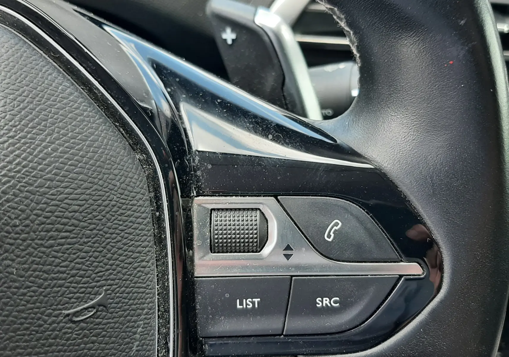 Gros plan sur les commandes gauche du volant noir du Peugeot 3008 gris, avec molette et boutons d'appel et audio.