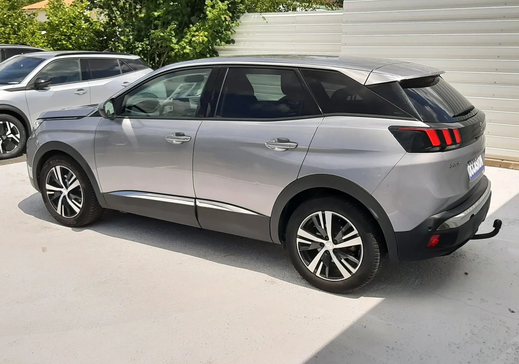 Peugeot 3008 gris en vue latérale droite, mettant en valeur ses feux arrière à trois griffes rouges et ses jantes bicolores.