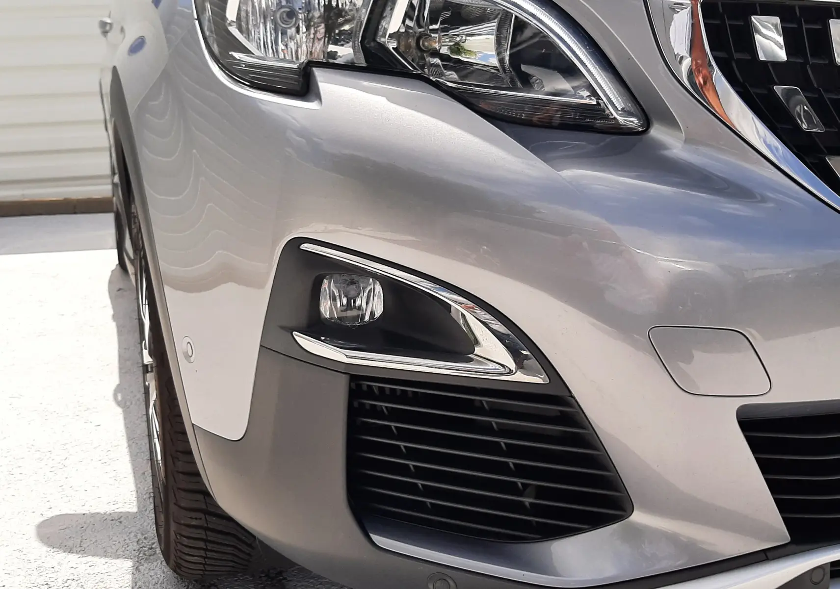 Gros plan sur l'avant droit gris d'un Peugeot 3008 2020, mettant en valeur le phare et la calandre chromée.