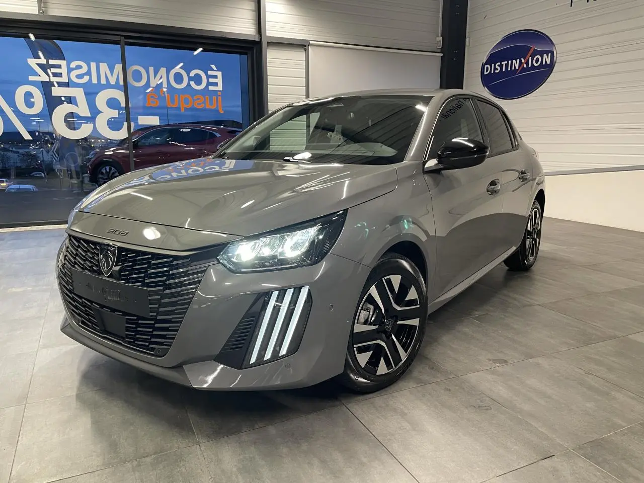 Peugeot 208 gris selenium vue 3/4 avant en intérieur, avec phares LED et jantes alliage bi-ton distinctives.