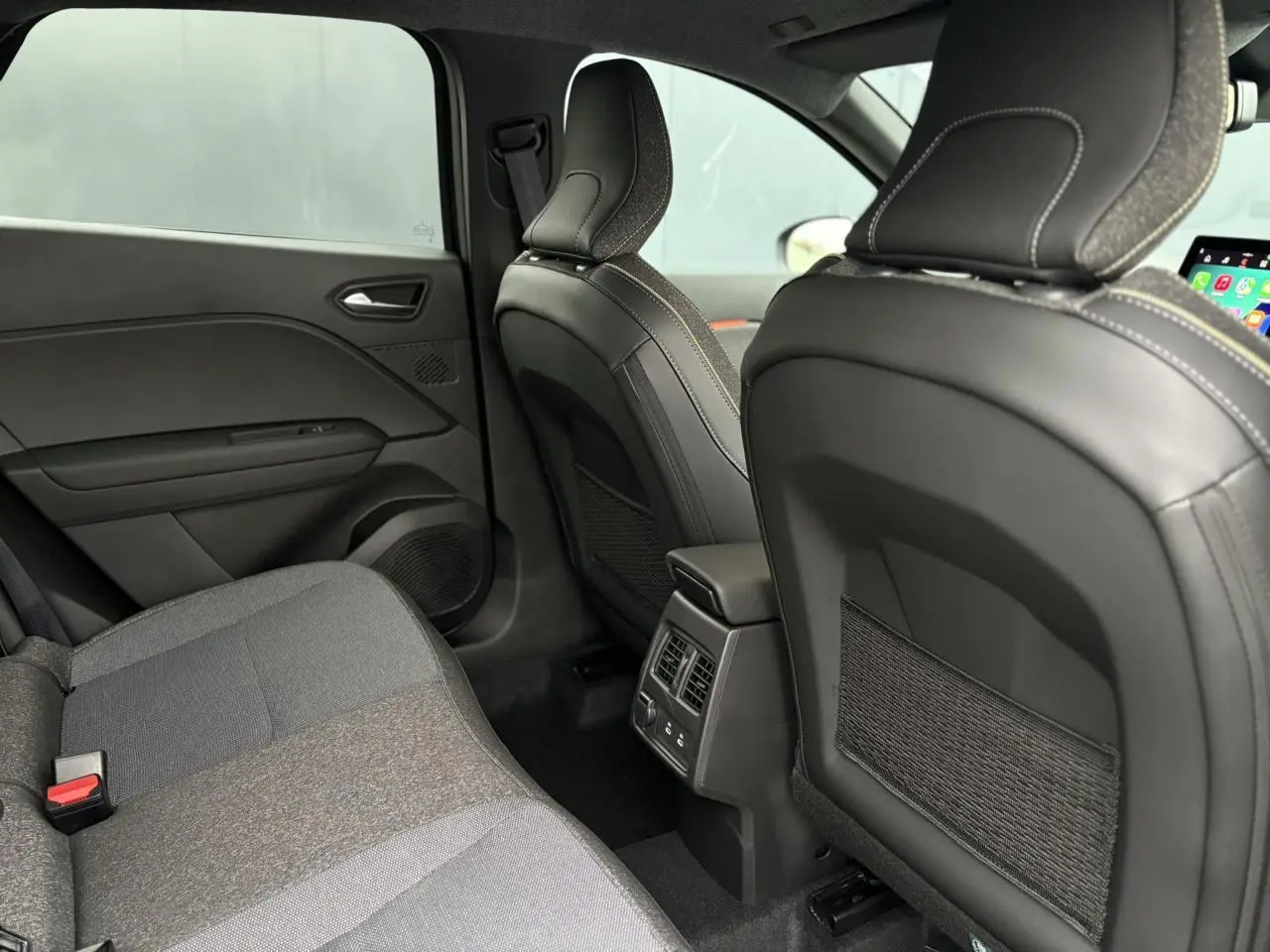 Vue intérieure arrière du Renault Captur 2025 montrant les sièges en tissu gris et la console centrale avec aérateurs et ports USB.