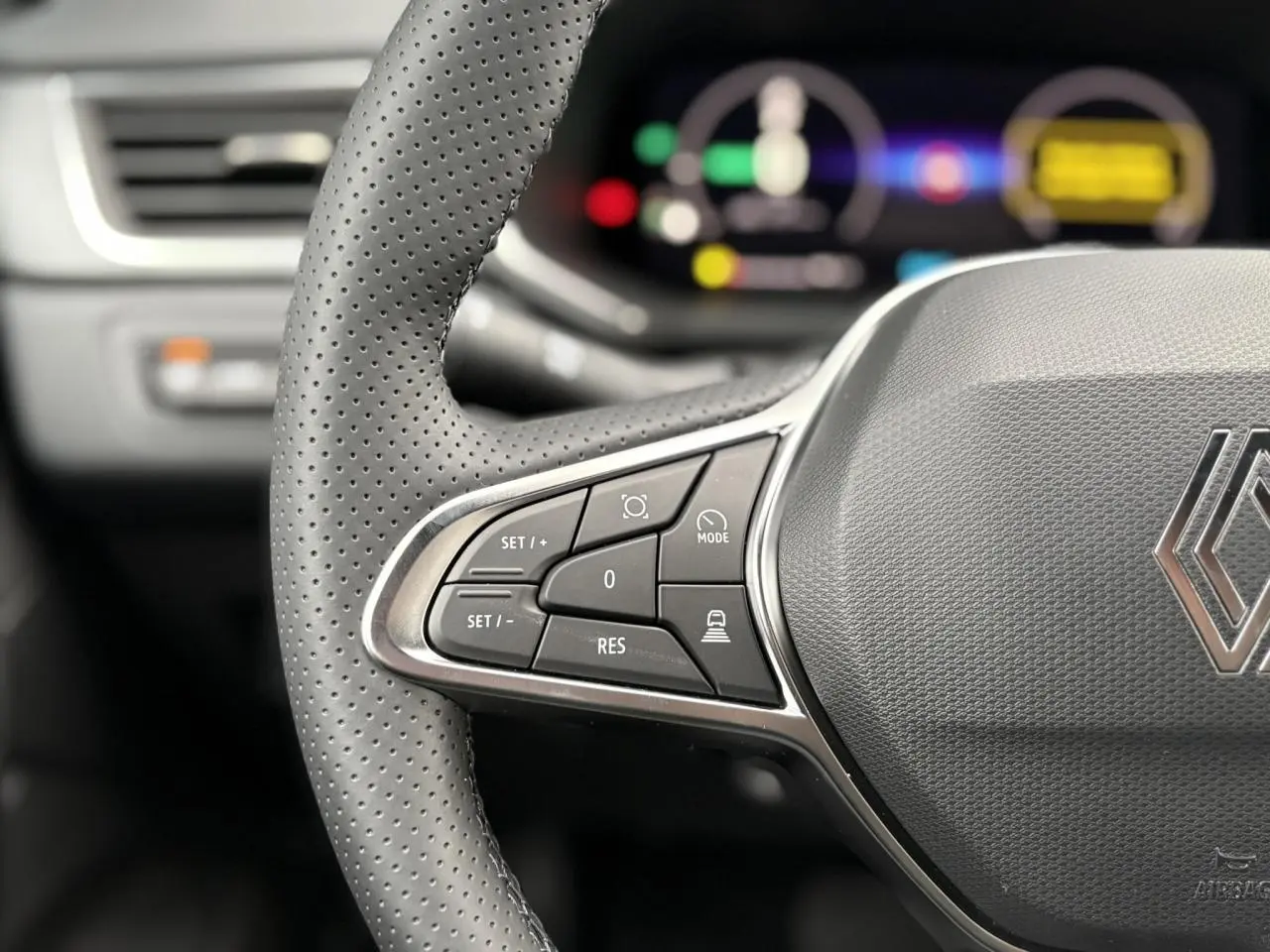 Gros plan sur le volant perforé noir du Renault Captur 2025 avec commandes intégrées et tableau de bord numérique flou.