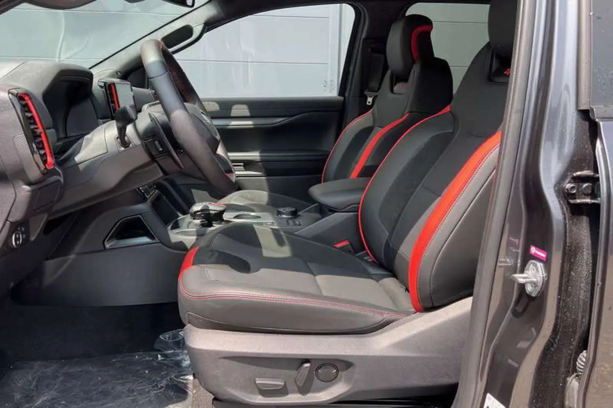 Vue intérieure côté gauche du Ford Ranger Raptor 2025, sièges sport noirs avec surpiqûres rouges et volant cuir multifonctions.