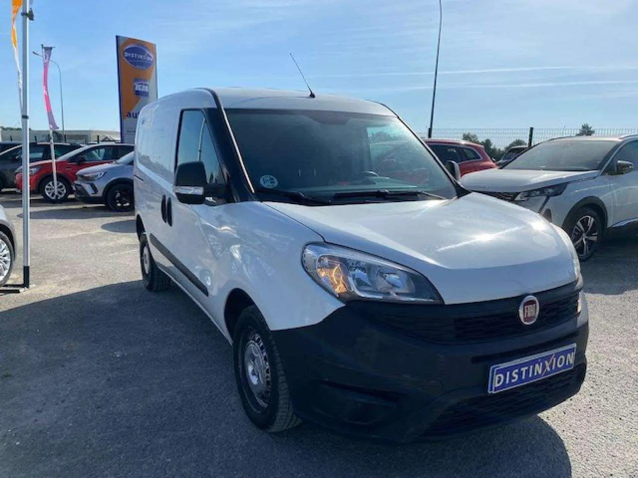 Fiat Doblo blanc vue 3/4 avant droit avec pare-chocs noir non peint et porte latérale droite visible.