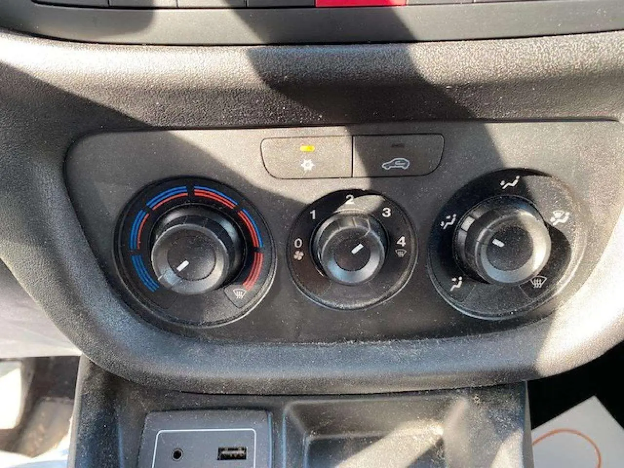 Gros plan sur les commandes de climatisation manuelle et la prise USB du tableau de bord du Fiat Doblo blanc de 2017.