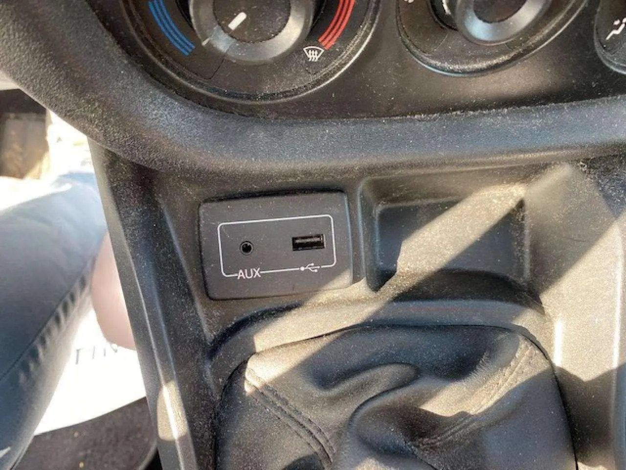Vue rapprochée de la console centrale du Fiat Doblo blanc, montrant la prise AUX, port USB et commande de climatisation.