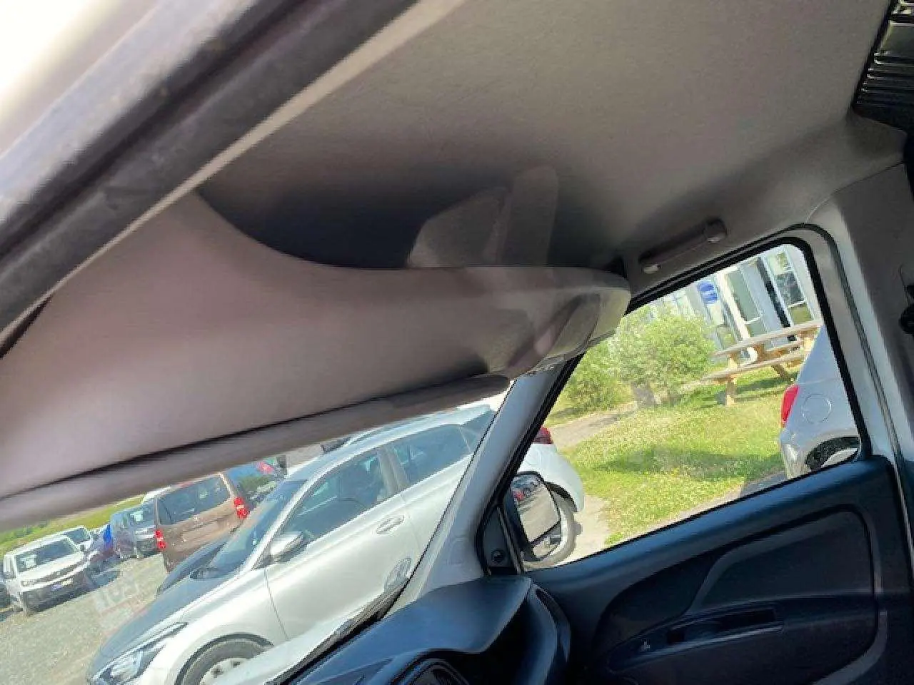 Vue intérieure côté conducteur du Fiat Doblo blanc, montrant le pare-soleil et la portière avec vitre.