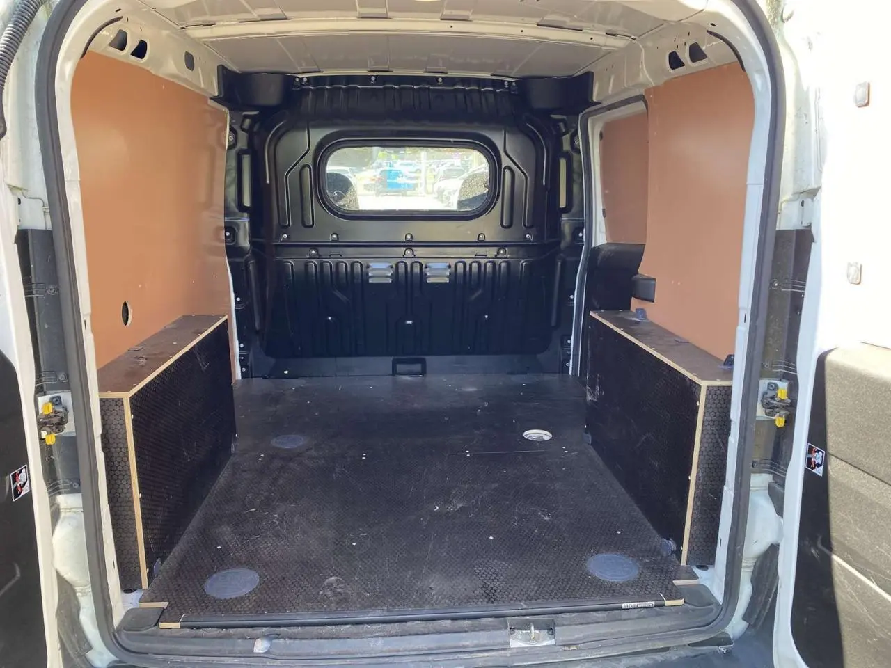 Vue intérieure arrière du fourgon blanc FIAT Doblo 2017 avec espace de chargement équipé d'un kit bois et paroi vitrée.