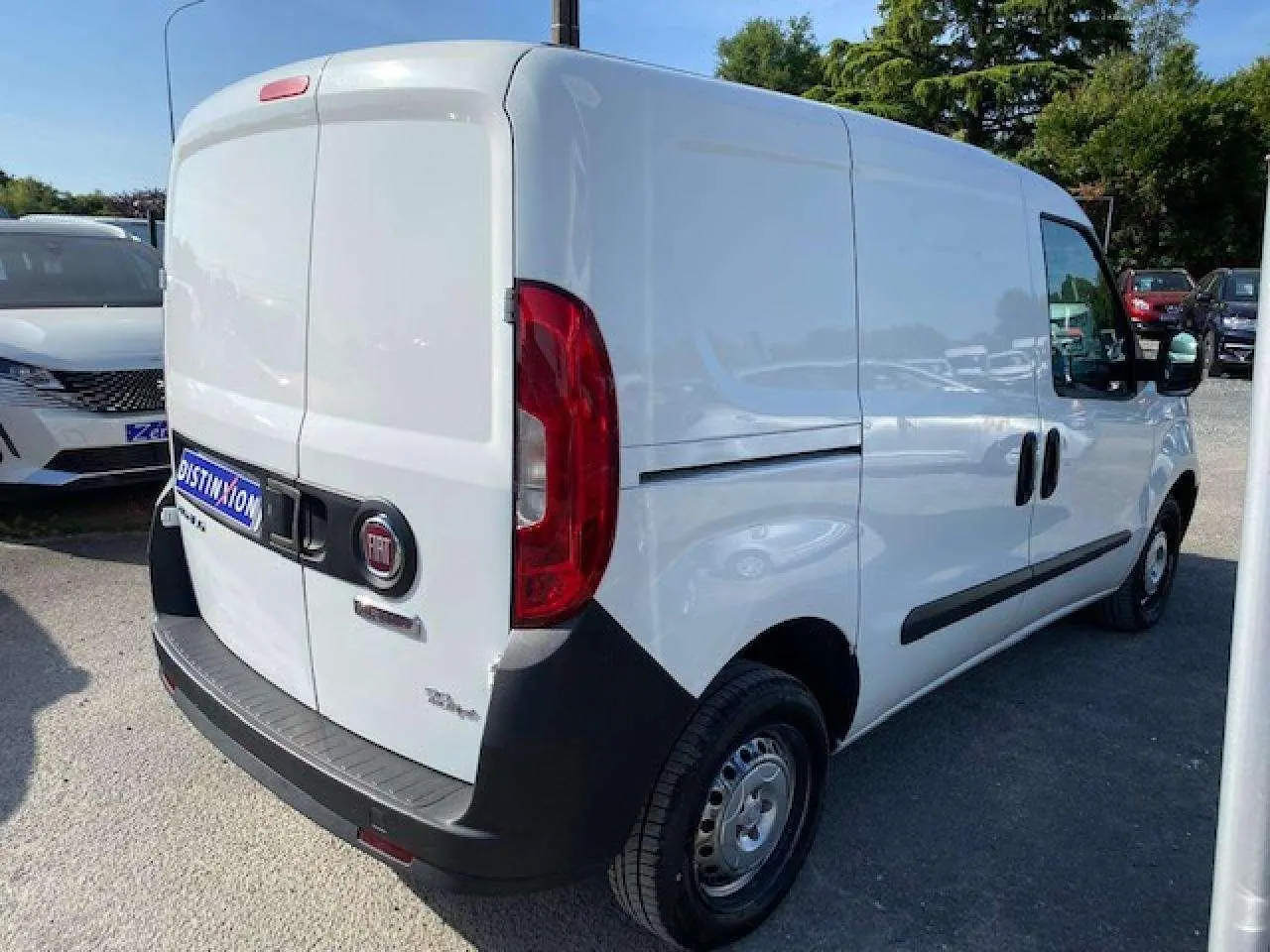 Fiat Doblo blanc vu en 3/4 arrière droit, fourgon tôlé avec pare-chocs noirs et porte latérale droite.