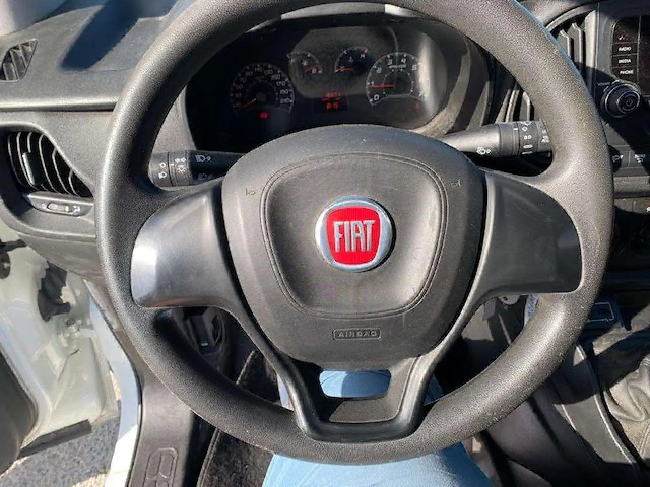 Vue rapprochée du volant noir avec logo rouge FIAT du fourgon blanc Doblo, tableau de bord et levier de vitesses visibles.