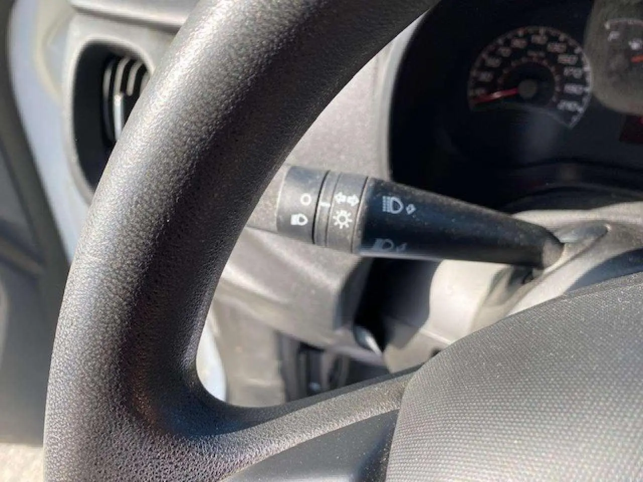 Gros plan sur le volant et la commande des phares du Fiat Doblo 2017, intérieur en plastique noir texturé.