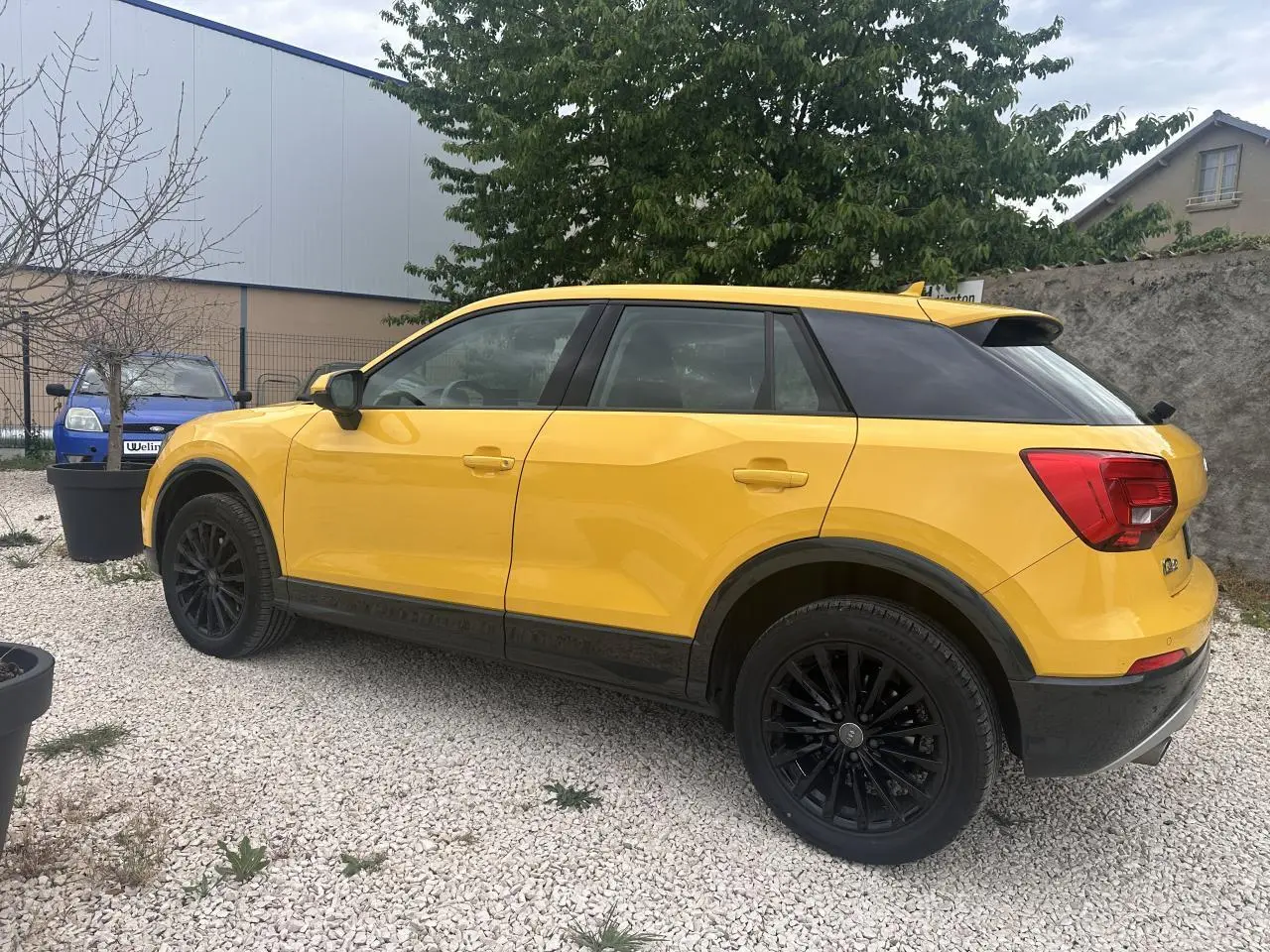 Audi Q2 jaune vue de profil côté gauche, avec jantes noires et toit noir contrastant visible en extérieur sur gravier.