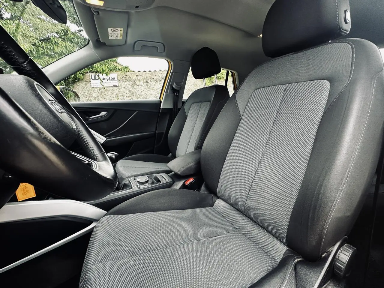 Vue intérieure côté conducteur de l'Audi Q2 1.6 TDI Business line 2017, sellerie tissu noir et gris, accoudoir central visible.
