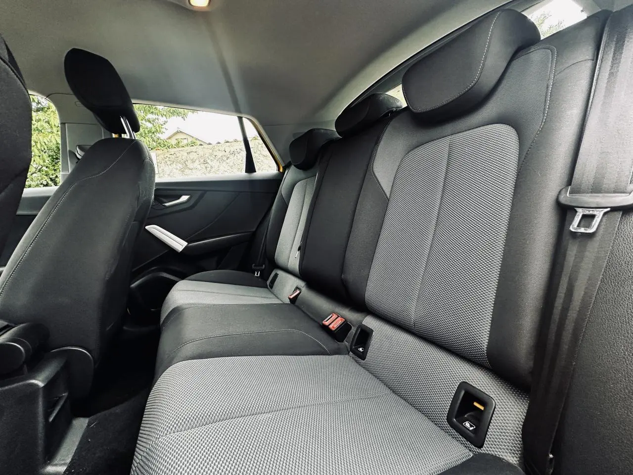Vue latérale intérieure montrant les sièges arrière gris et noirs de l'Audi Q2 1.6 TDI Business line jaune.