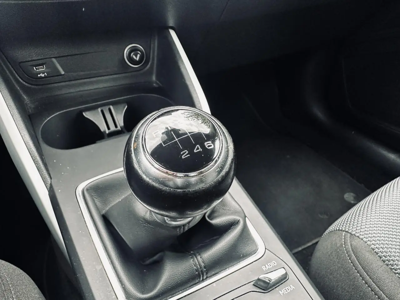 Gros plan sur le levier de vitesses manuel noir de l'Audi Q2, avec console centrale et siège tissu gris visibles.