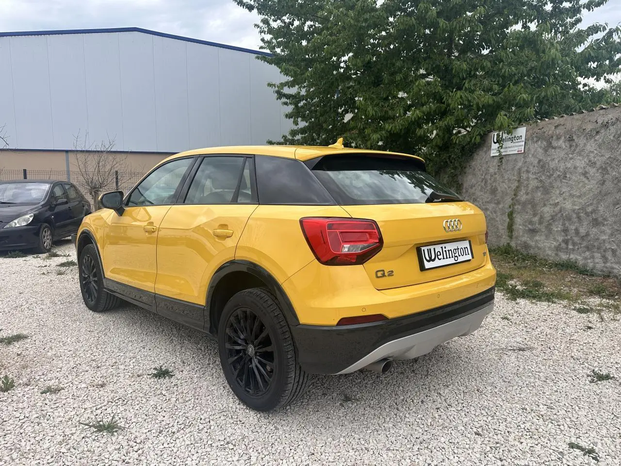 Audi Q2 jaune vue 3/4 arrière droit, avec jantes noires et détails noirs sur pare-chocs et bas de caisse.