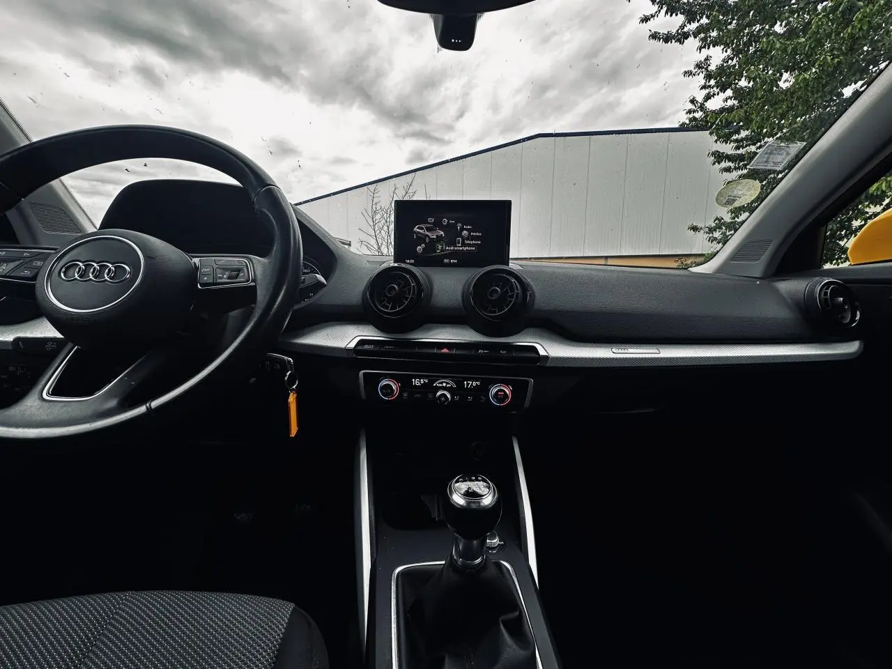 Vue intérieure avant de l'Audi Q2 jaune 2017, mettant en valeur le volant cuir, la boîte manuelle et l'écran central.