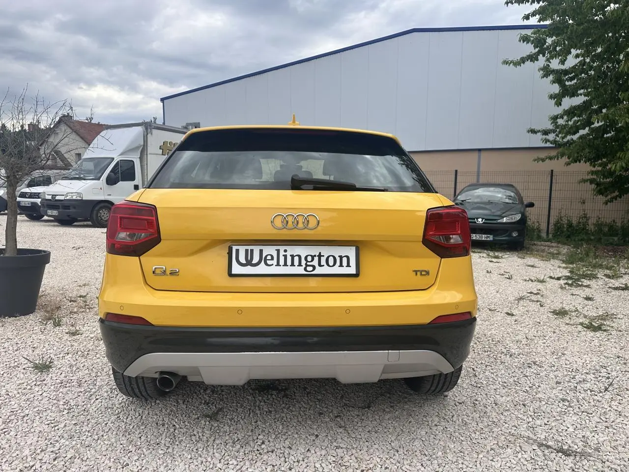 Vue arrière d'un Audi Q2 jaune avec feux rouges et sortie d'échappement chromée visible sur un sol gravillonné.