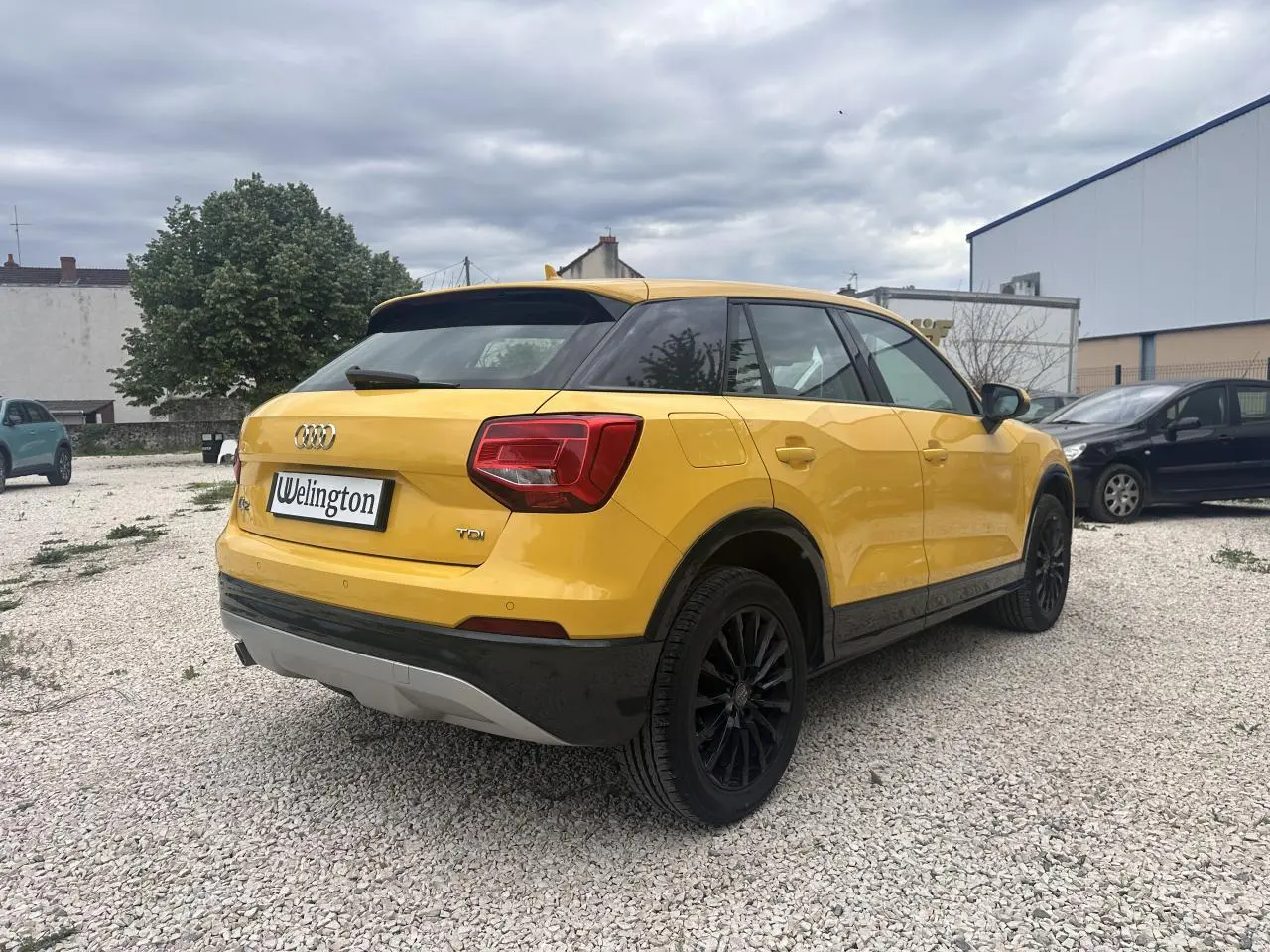 Audi Q2 jaune vue 3/4 arrière droit, jantes noires et toit noir contrastant sur un sol gravillonné.
