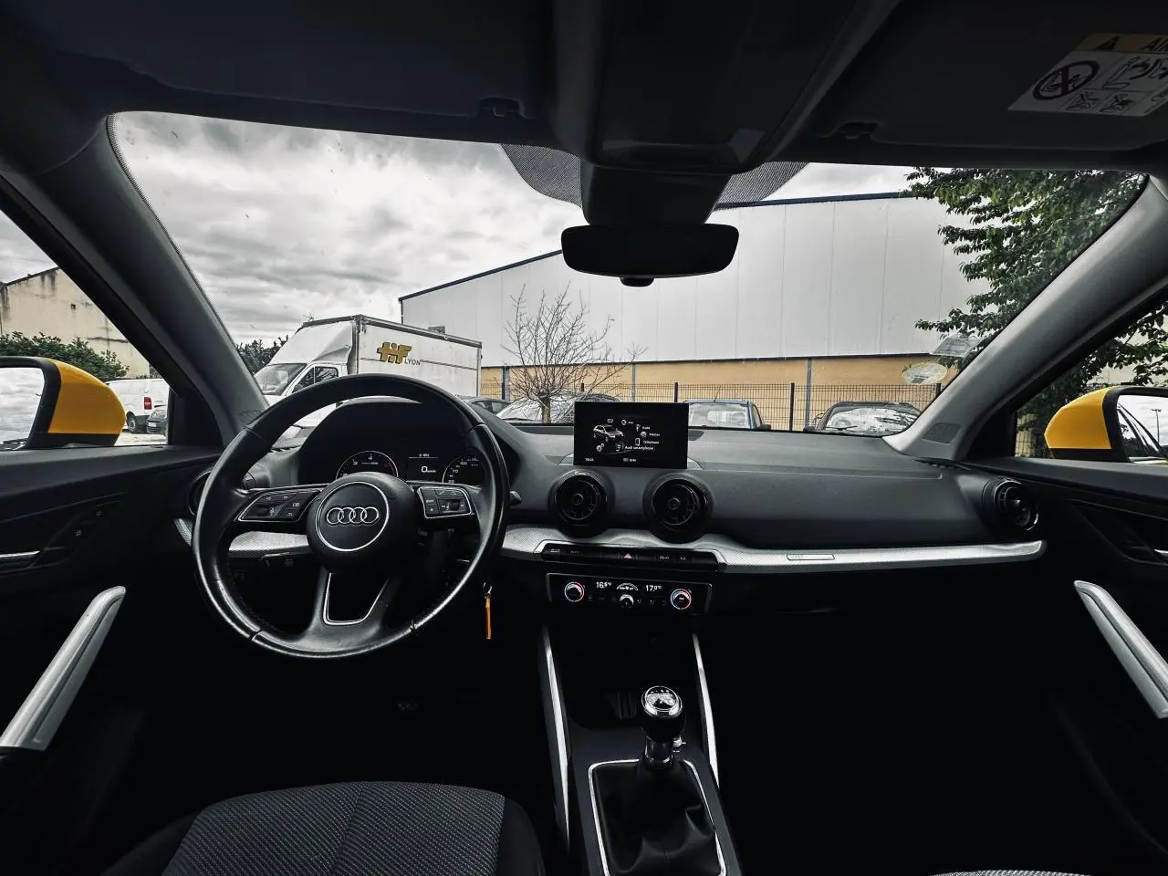 Vue intérieure avant de l'Audi Q2 jaune, volant multifonction, tableau de bord moderne avec écran central et boîte manuelle.