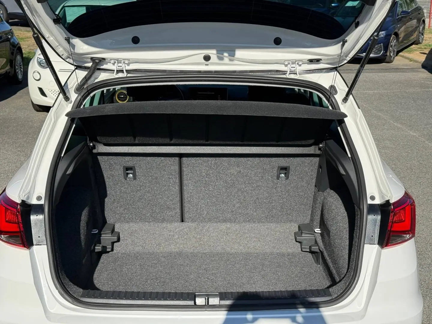 Coffre ouvert vu de l’arrière d’un SEAT Arona blanc Candy avec cache-bagages noir et intérieur gris.