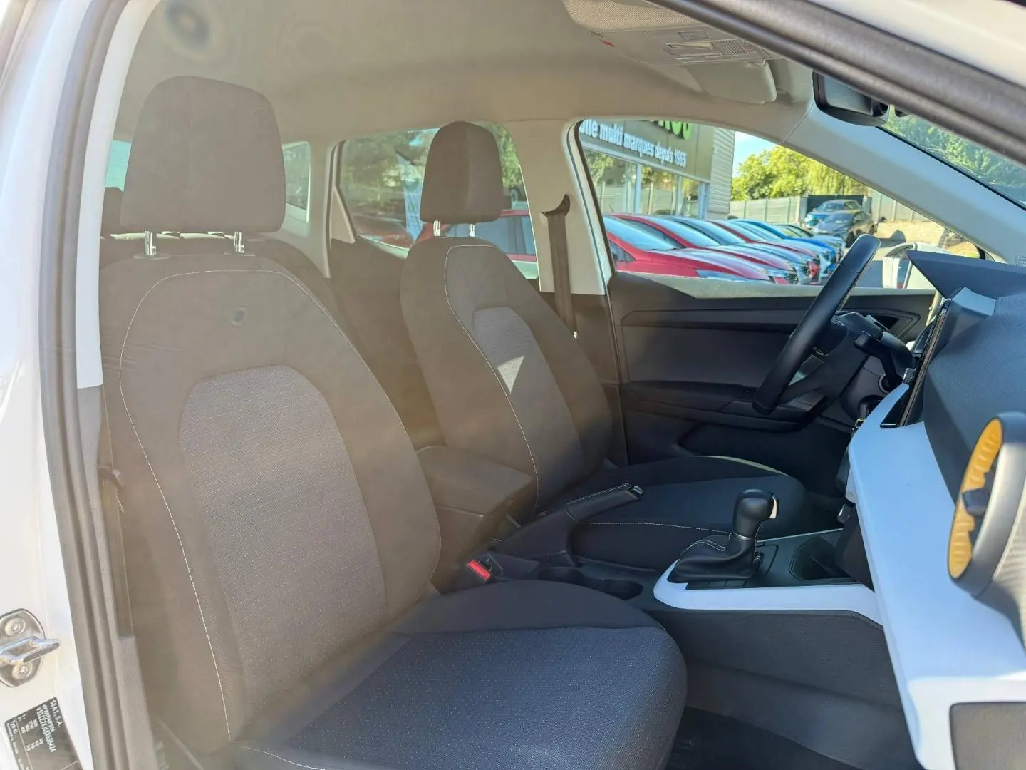 Vue intérieure côté gauche du SEAT Arona 2025, sièges tissu gris et console centrale avec levier de boîte auto.