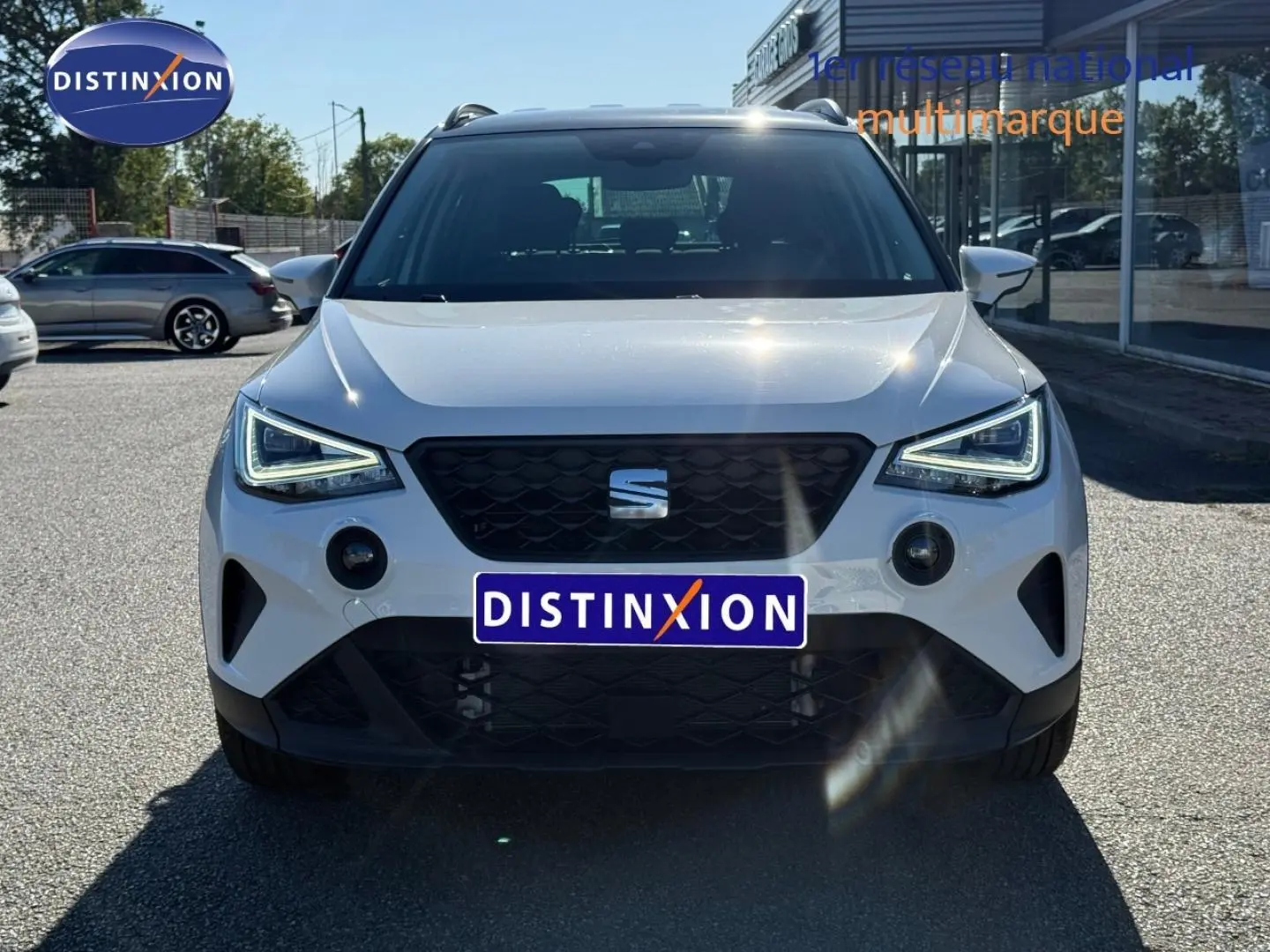 Vue frontale d'un SEAT Arona blanc Candy avec toit noir, feux LED allumés et calandre noire distinctive.