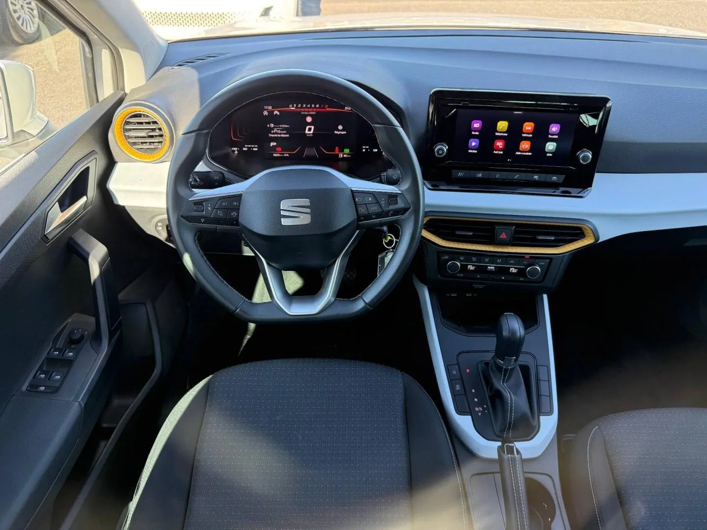 Vue intérieure avant du tableau de bord de la SEAT Arona 2025 avec volant cuir, écran tactile et accents jaunes autour des aérateurs.
